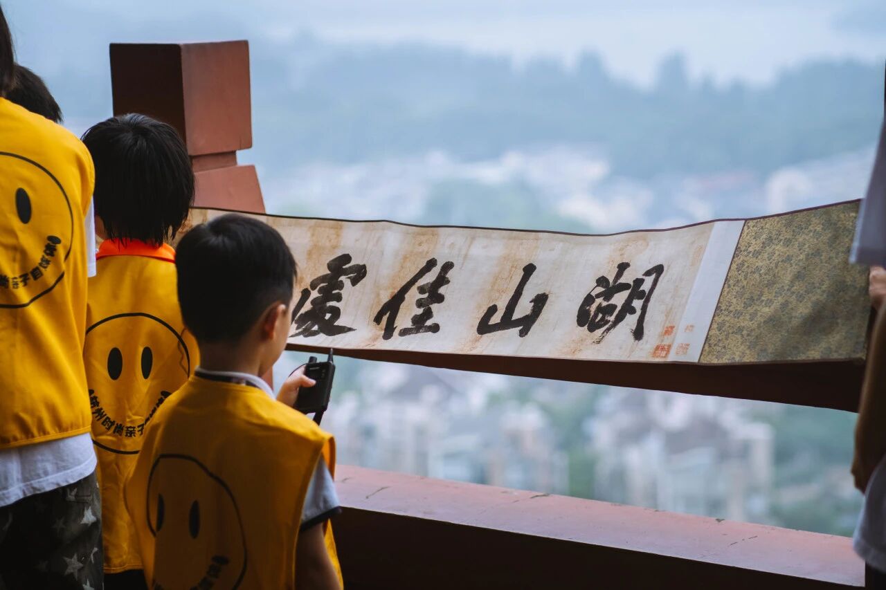 穿黄色笑脸背心的孩子在高处观景台看湖山佳处书法，浸思研学文化走读实拍