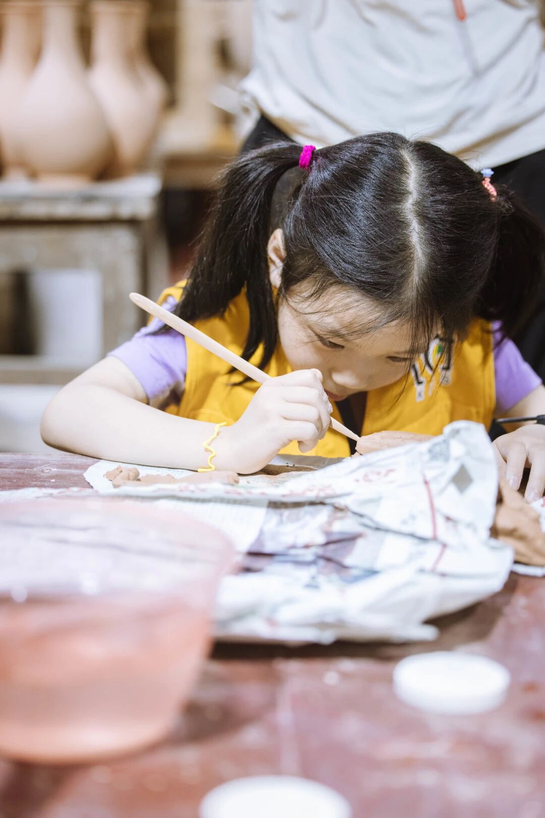扎双马尾的小女孩在陶艺教室专注绘画，浸思研学室内手作课程