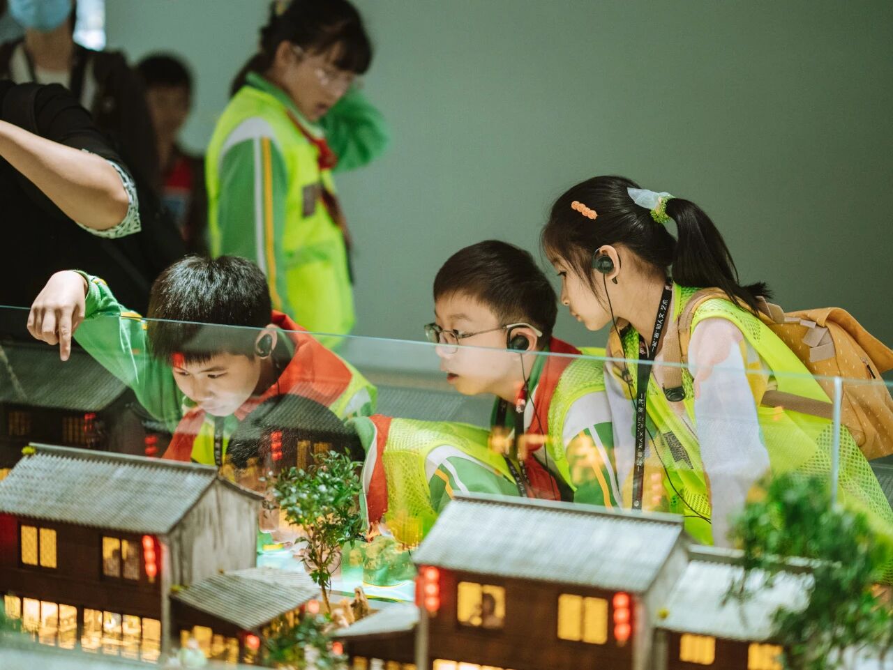 穿统一马甲的学生在室内聚精会神参观微缩建筑模型展览，浸思研学基地工厂课程