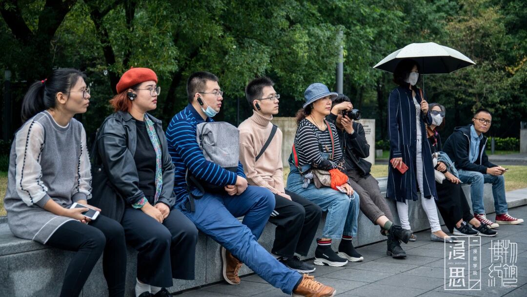 一群人在户外绿树成荫的长椅上休息，浸思研学户外研学实拍