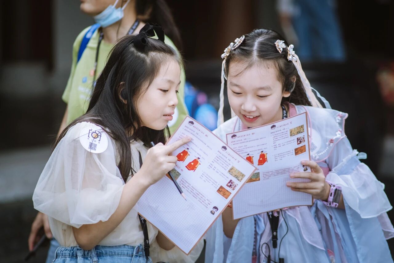 两个小女孩在户外专注查看活动手册地图，浸思研学户外探索实拍